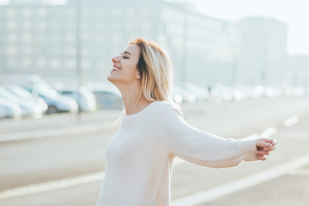 Half length of young beautiful cacuasian woman feeling free with arms wide open in the city back light - liberty, freedom, girl power concept